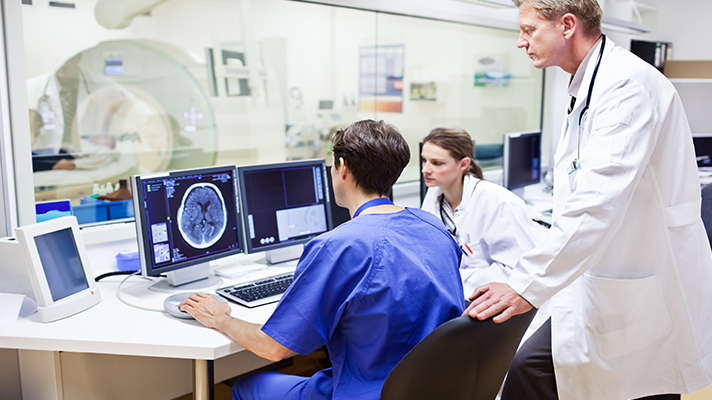 Doctor talking to radiologists at a computer with an MRI machine in the background.