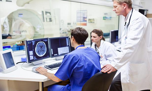 Doctor talking to radiologists at a computer with an MRI machine in the background.